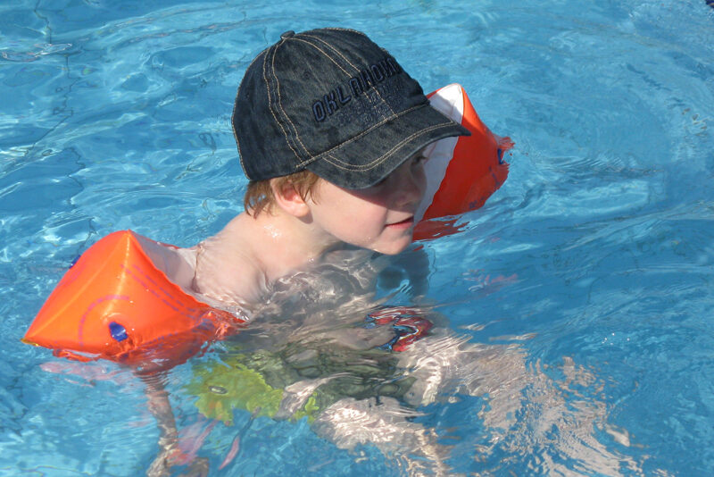 Kind mit Schwimmflügerl und Kappe im Wasser