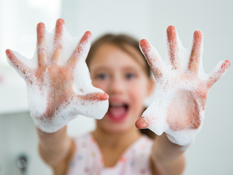ein Mädchen streckt ihre mit Seifenschaum bedeckten Hände Richtung Kamera