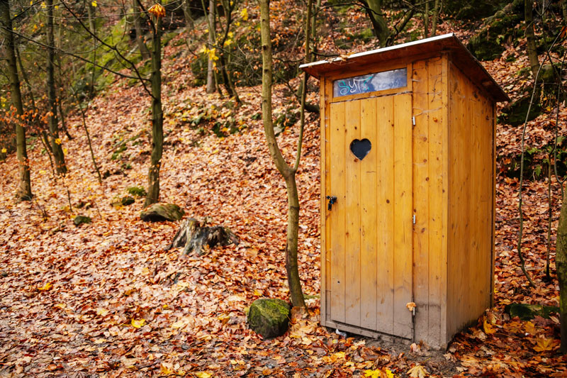 WC-Kabine aus Holz neben Waldweg