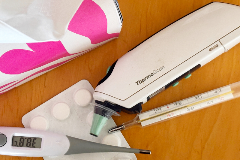 3 unterschiedliche Fiebermesser, eine angebrochene Blisterpackung Tablettenund die Ecke einer Taschentuchbox