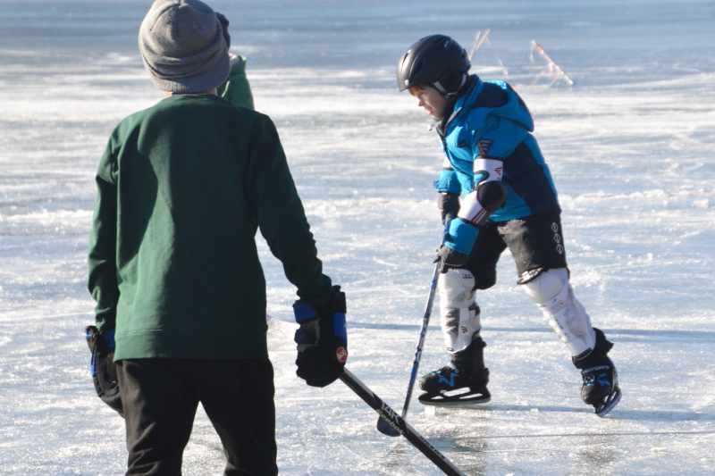 Zwei Kinder spielen am gefrorenen See Eishockey